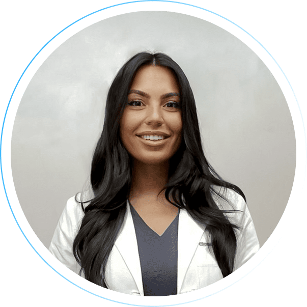 Smiling woman with long dark hair in a white coat against light background.